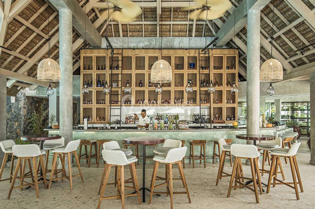 Bar moderne avec comptoir en marbre, étagères en bois remplies de bouteilles, et chaises hautes dans un espace lumineux.