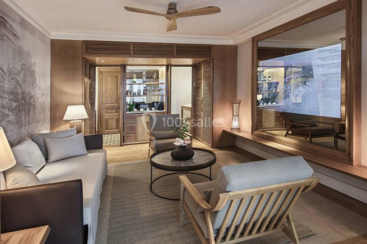 Salon lumineux avec mobilier en bois clair, canapé, fauteuils, table basse et grand miroir mural.