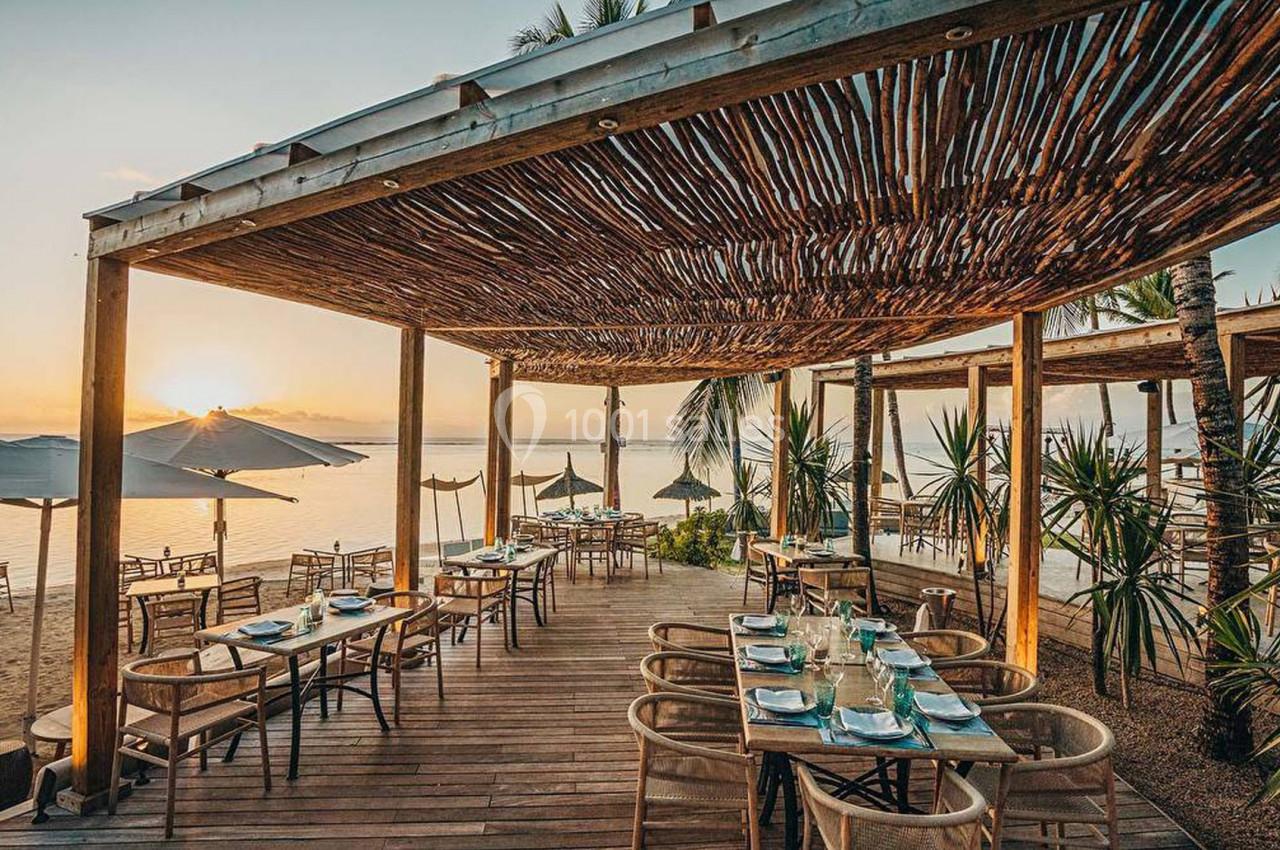 Terrasse en bois d'un restaurant en bord de mer, avec des tables dressées et vue sur le coucher de soleil.