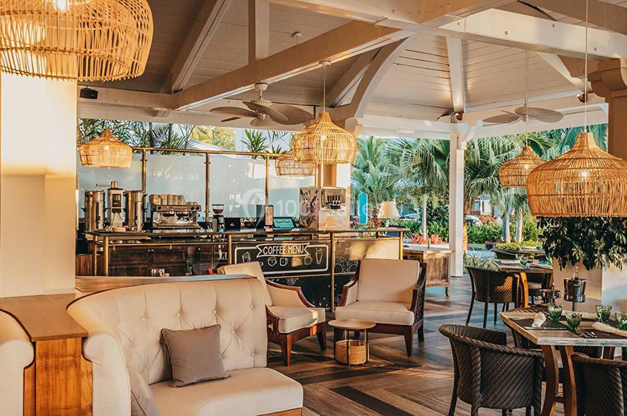 Intérieur lumineux d'un café avec mobilier en bois, luminaires en rotin et vue sur un jardin tropical.