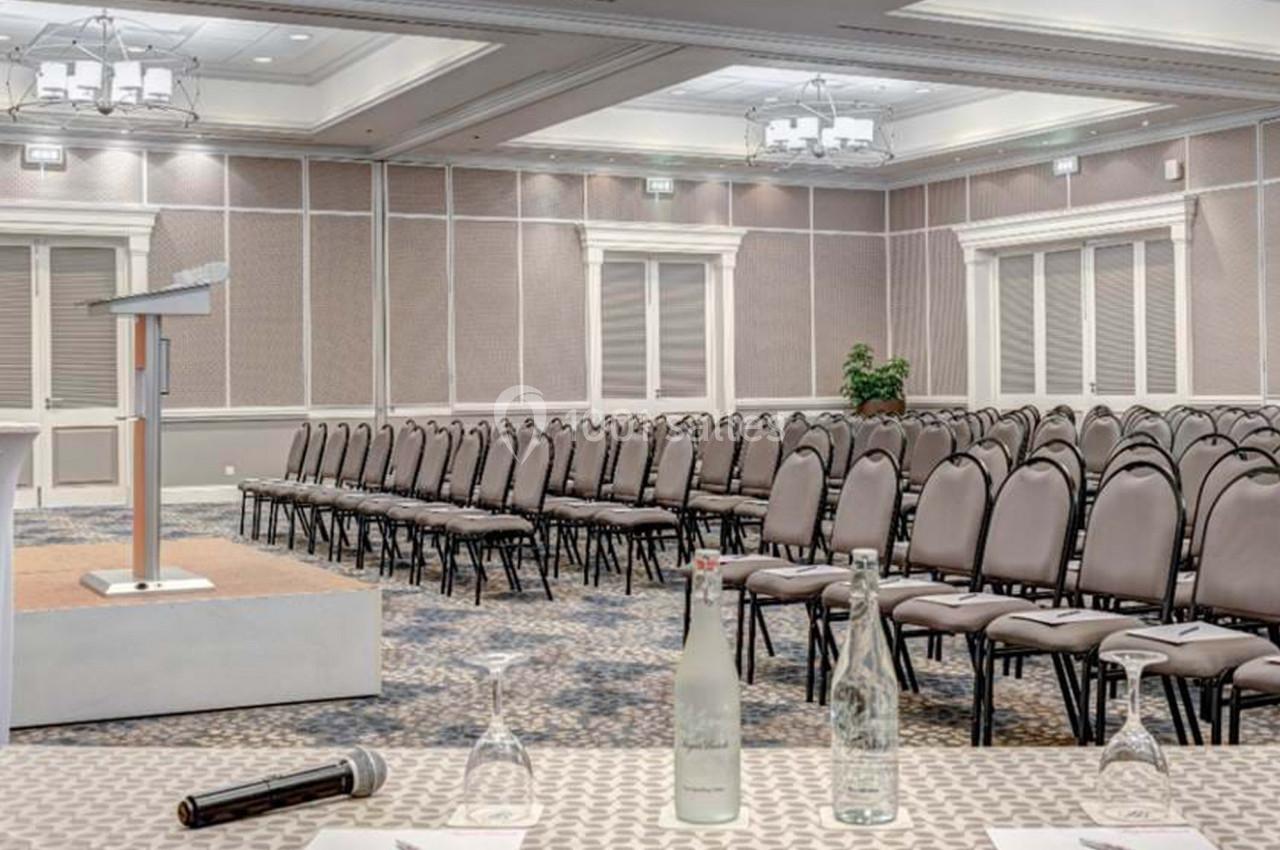 Salle de conférence vide avec rangées de chaises alignées, un pupitre sur une estrade et des bouteilles d'eau sur une table…