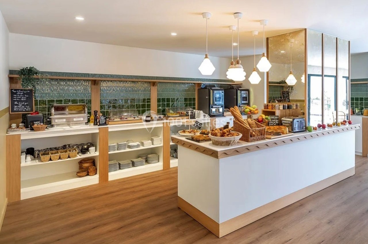 Buffet de petit-déjeuner avec viennoiseries, fruits, boissons et équipements dans une salle lumineuse au sol en bois.