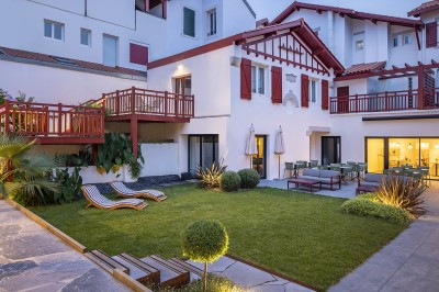 Vue d'une cour intérieure avec balcons en bois rouge, grandes baies vitrées et éclairage chaleureux au crépuscule.
