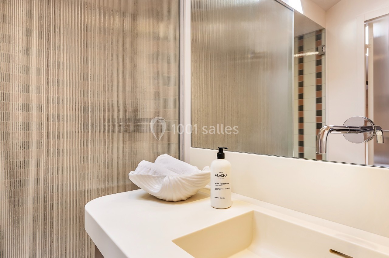 Lavabo moderne avec un distributeur de savon blanc et une serviette pliée dans une salle de bain lumineuse.