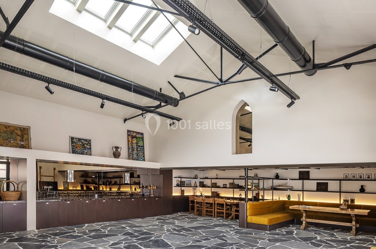 Intérieur spacieux avec sol en pierre, plafond industriel, puits de lumière et mobilier en bois dans un espace lumineux.
