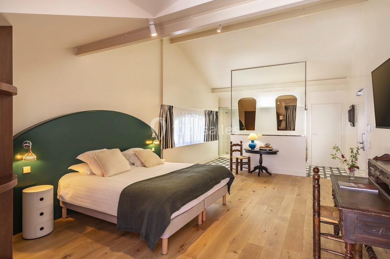 Chambre lumineuse avec lit double, parquet en bois clair, bureau, miroir mural et décoration sobre.