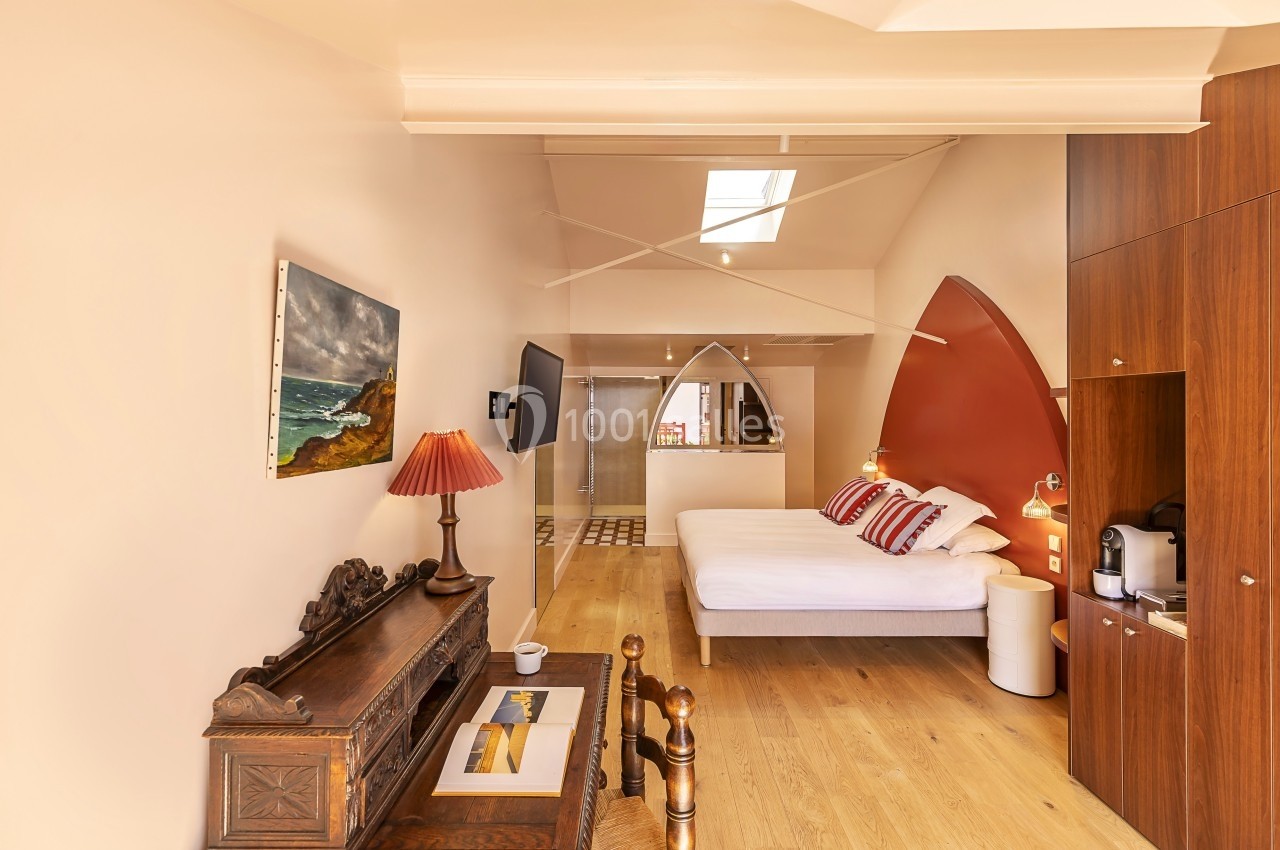 Chambre lumineuse avec lit double, mobilier en bois, lampe de chevet, tableau mural et salle de bain attenante.