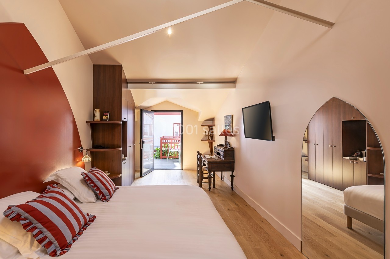 Chambre lumineuse avec lit double, bureau, télévision murale et accès à un balcon, décorée dans des tons chauds.