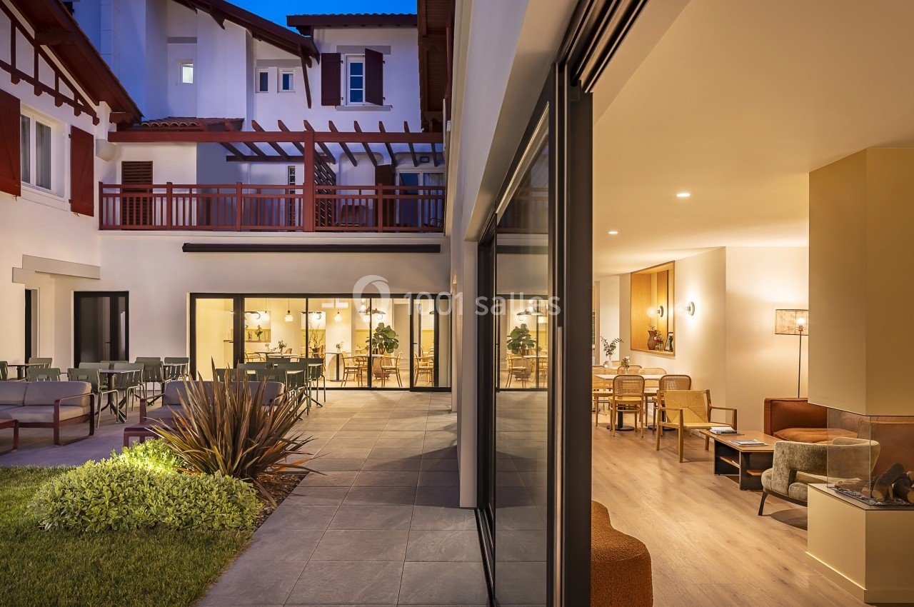 Cour intérieure d'un bâtiment moderne avec terrasse aménagée, vue sur des espaces intérieurs éclairés en soirée.