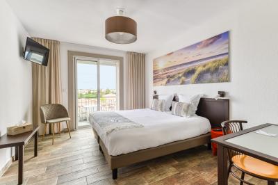 Chambre lumineuse avec lit double, tableau mural, télévision, balcon et mobilier simple sur un sol en parquet.