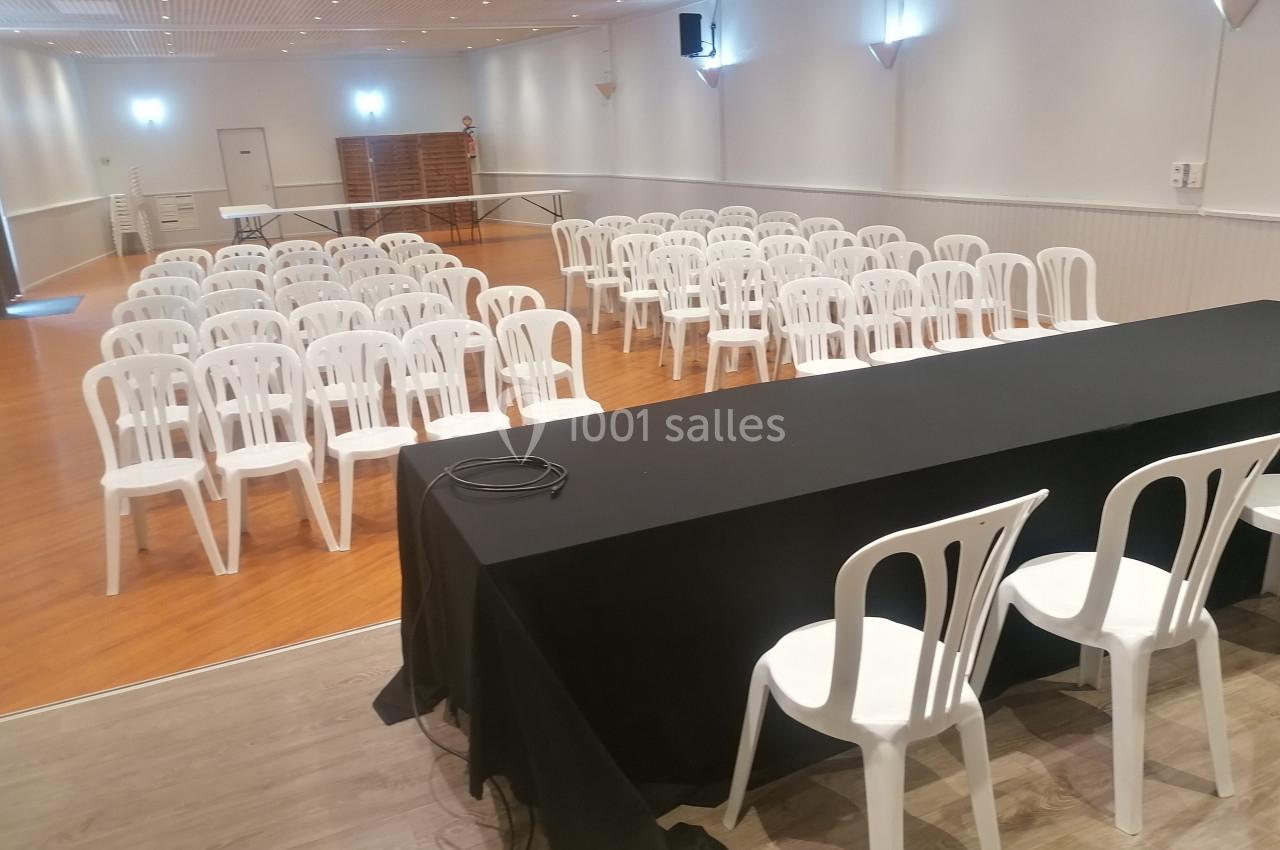 Salle de conférence avec des rangées de chaises blanches alignées face à une table recouverte d'une nappe noire.