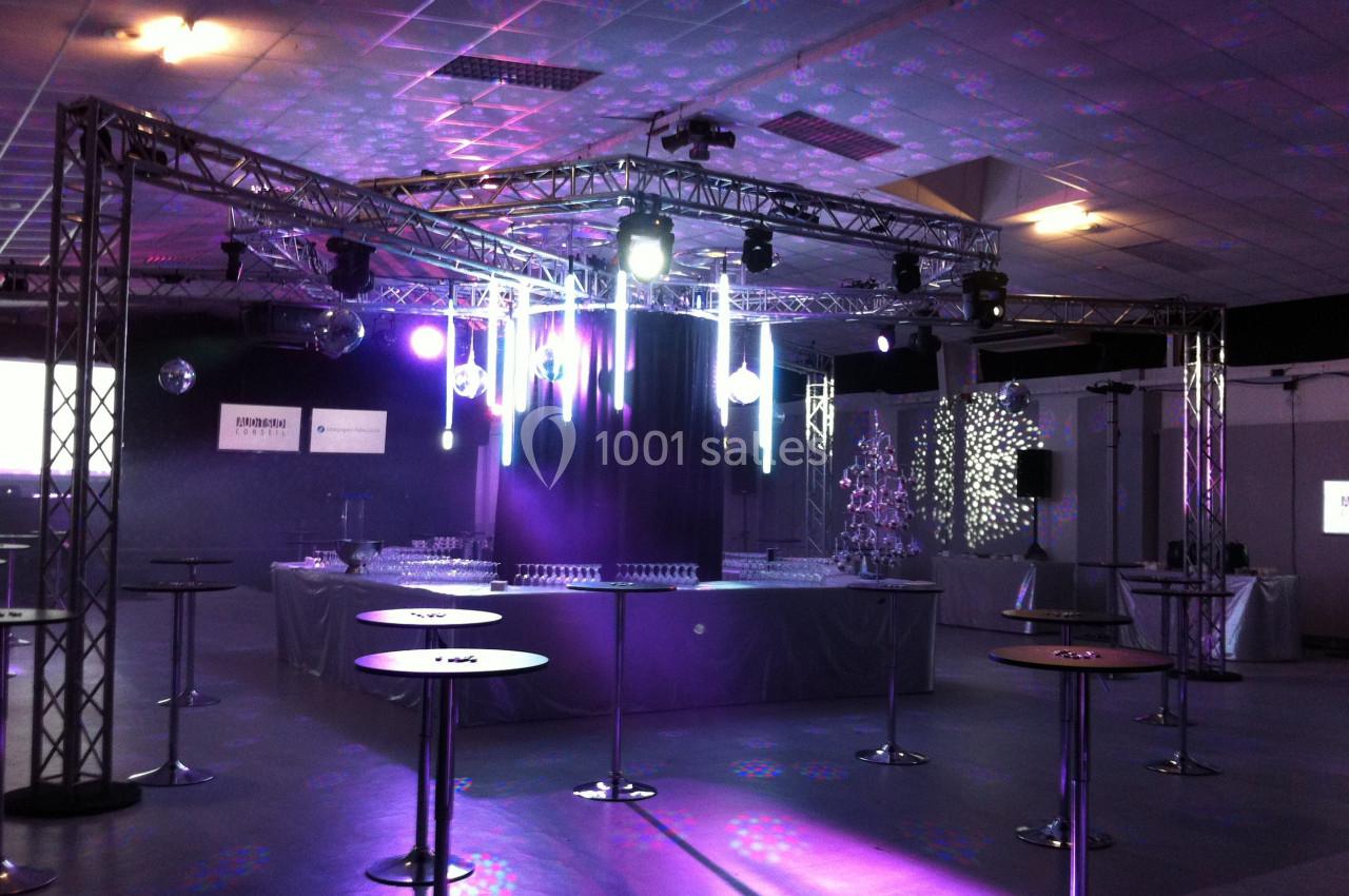 Salle de réception avec éclairage coloré, tables hautes et structure métallique pour les lumières.