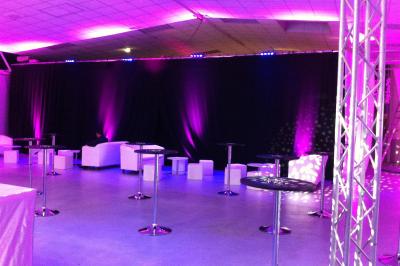 Salle de conférence avec des rangées de chaises blanches en plastique, un podium et un écran de projection.