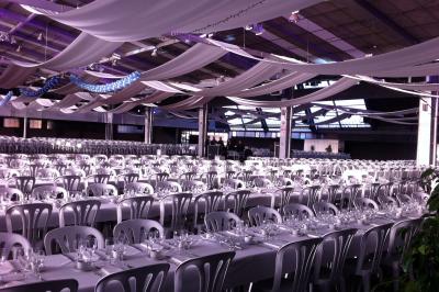 Salle de conférence avec des rangées de chaises blanches en plastique, un podium et un écran de projection.