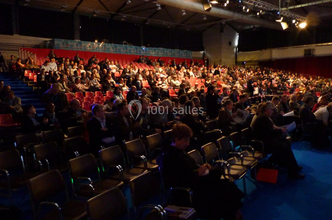 Salle de conférence remplie de participants assis, éclairée par des projecteurs, avec des rangées de sièges vides au premier…