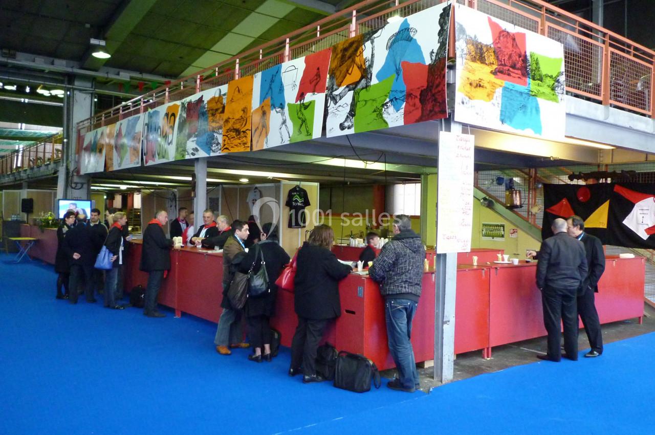 Des personnes discutent et prennent des boissons à un comptoir rouge dans un espace intérieur avec une mezzanine décorée.