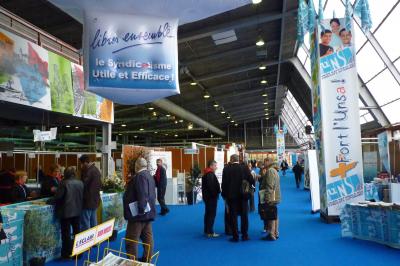 Salle de conférence avec des rangées de chaises blanches en plastique, un podium et un écran de projection.