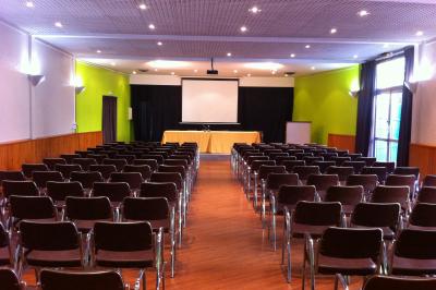 Salle de conférence avec des rangées de chaises blanches en plastique, un podium et un écran de projection.
