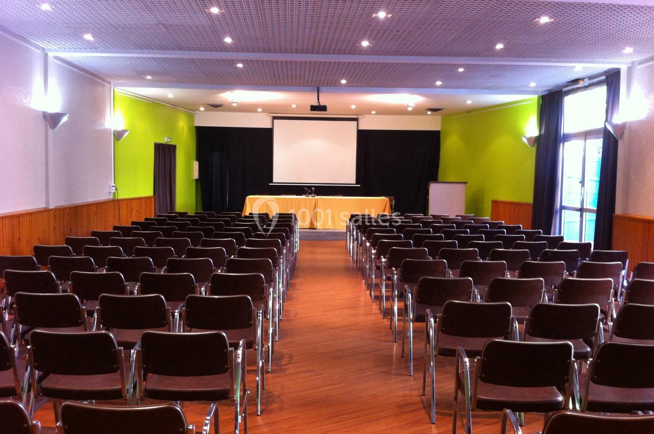 Salle de conférence avec rangées de chaises vides, écran de projection et table installée à l'avant.