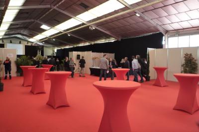 Salle de conférence avec des rangées de chaises blanches en plastique, un podium et un écran de projection.
