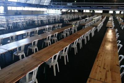 Salle de conférence avec des rangées de chaises blanches en plastique, un podium et un écran de projection.