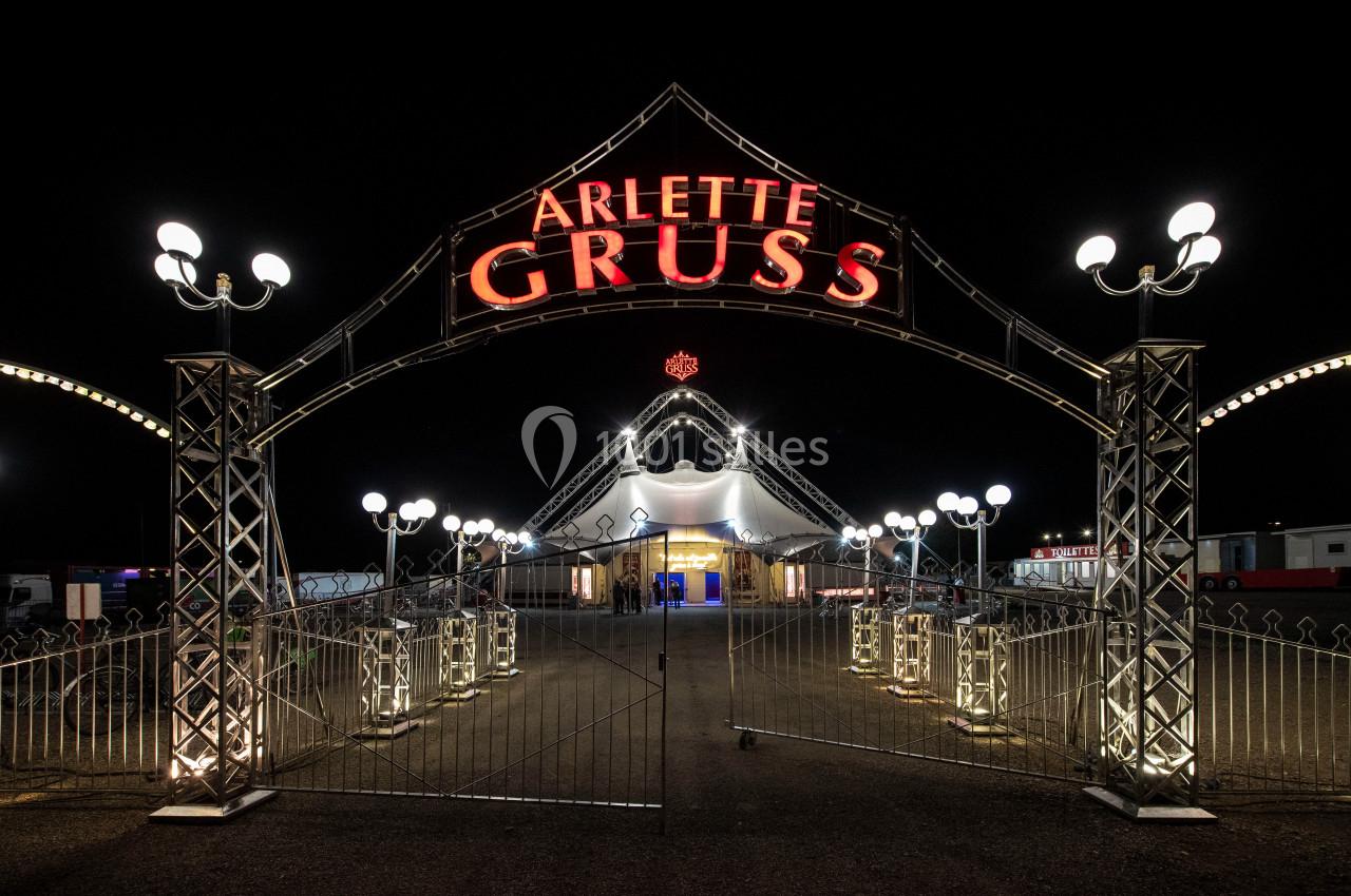 Entrée illuminée d'un chapiteau de cirque avec une arche métallique portant l'inscription ’Arlette Gruss’.