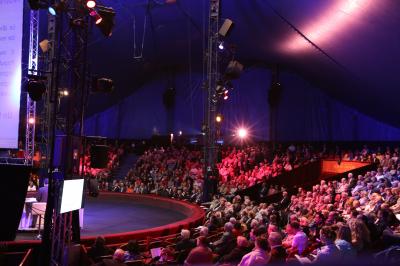 Salle de spectacle circulaire avec gradins éclairés par des lumières violettes et une scène centrale.