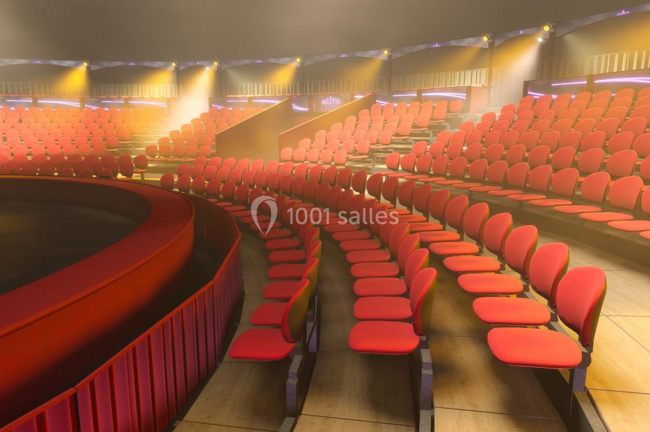 Gradins circulaires avec des sièges rouges vides dans une salle éclairée, entourant une scène centrale.