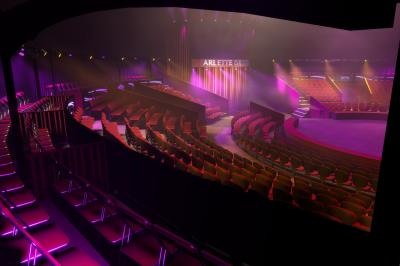 Salle de spectacle circulaire avec gradins éclairés par des lumières violettes et une scène centrale.