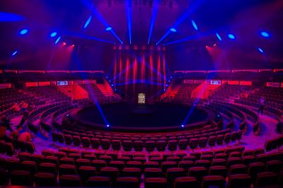 Salle de spectacle circulaire avec gradins éclairés par des lumières violettes et une scène centrale.