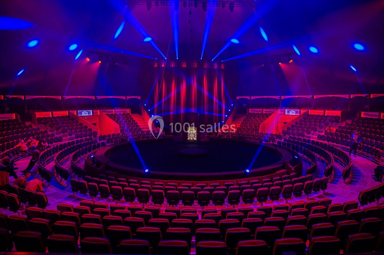 Gradins circulaires illuminés de lumières rouges et bleues entourant une scène centrale dans une salle de spectacle.