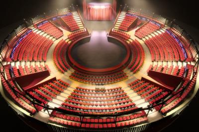 Salle de spectacle circulaire avec gradins éclairés par des lumières violettes et une scène centrale.