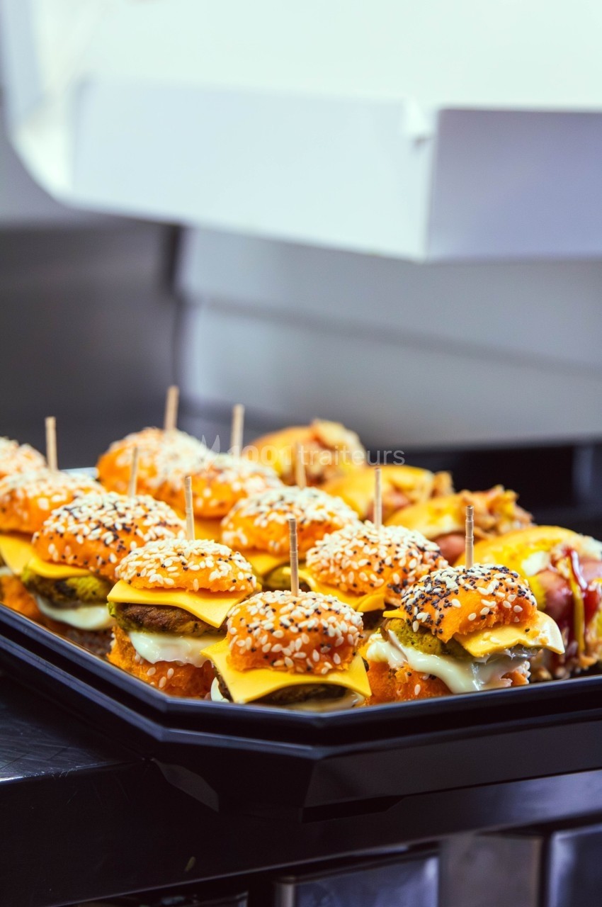 Plateau de mini-burgers garnis de fromage, servis avec des piques en bois, posé sur un plan de travail en cuisine.