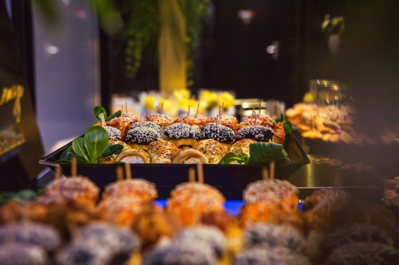 Plateau de mini-burgers variés garnis de graines et de légumes, présenté sur une table lors d'un buffet.