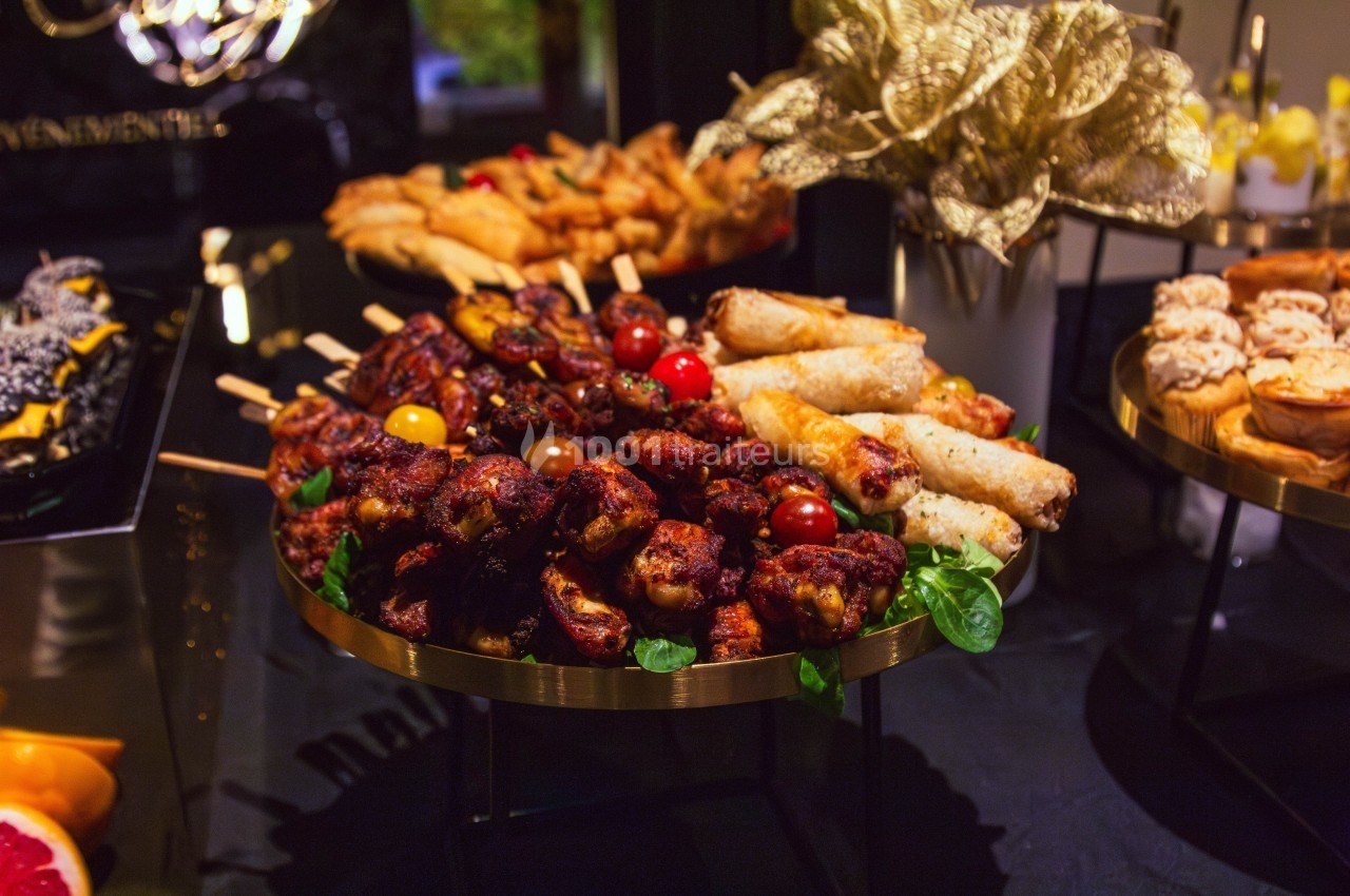 Plateau de brochettes de viande grillée, rouleaux croustillants et autres amuse-bouches sur une table de buffet.