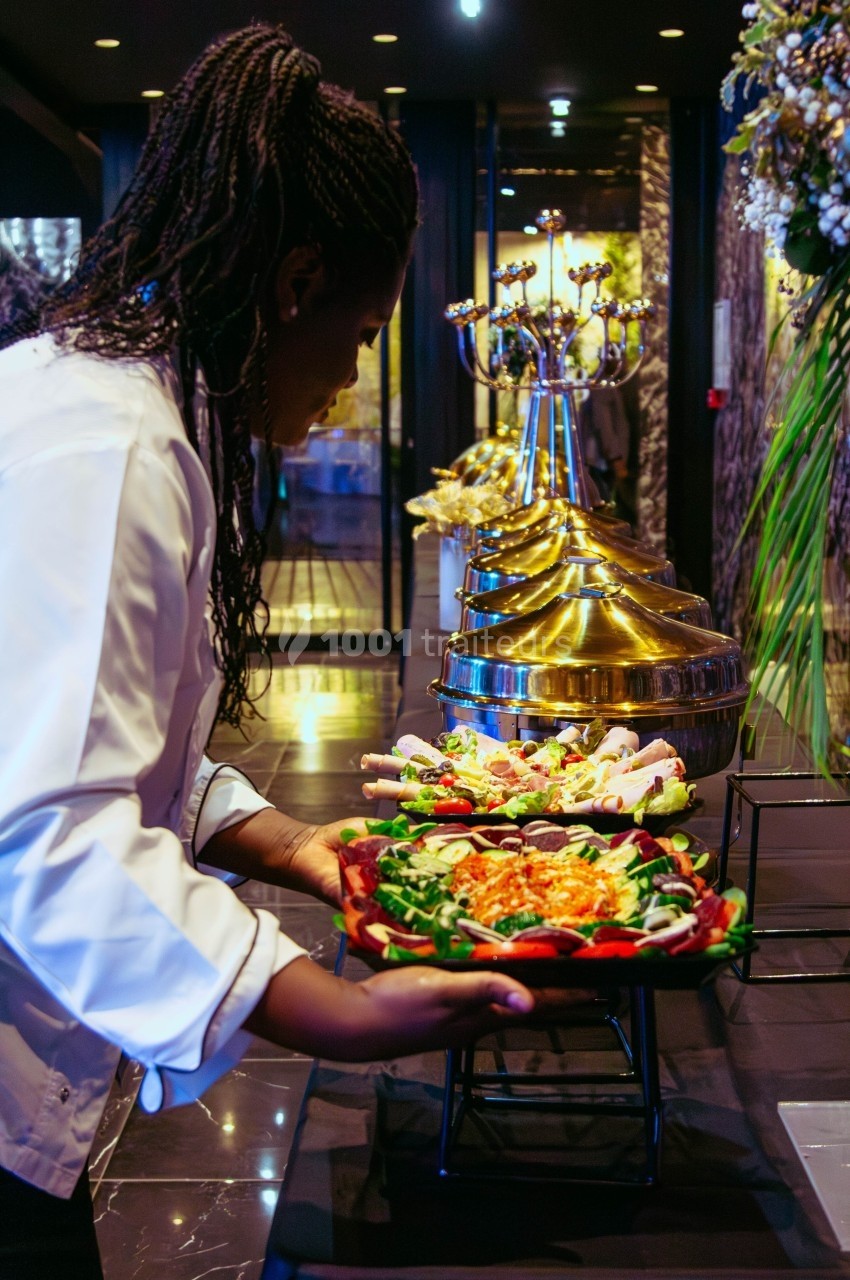 Une cheffe dispose des plats garnis de légumes frais sur une table de buffet dans un cadre élégant.