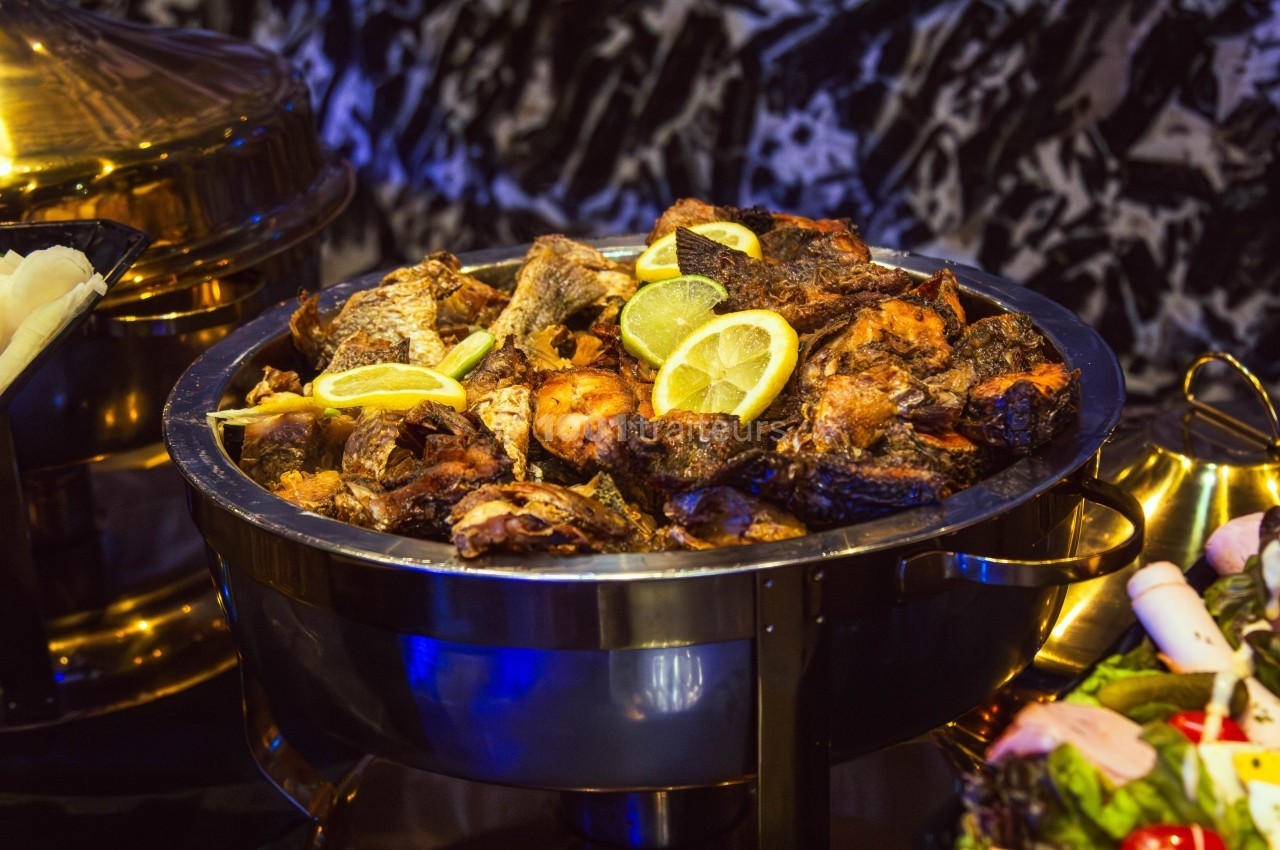 Plat de poissons grillés garnis de tranches de citron, présenté dans un récipient en métal sur une table.