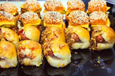 Plateau de mini-sandwichs variés, garnis de fromage, viande hachée et saucisses, présentés sur une table.