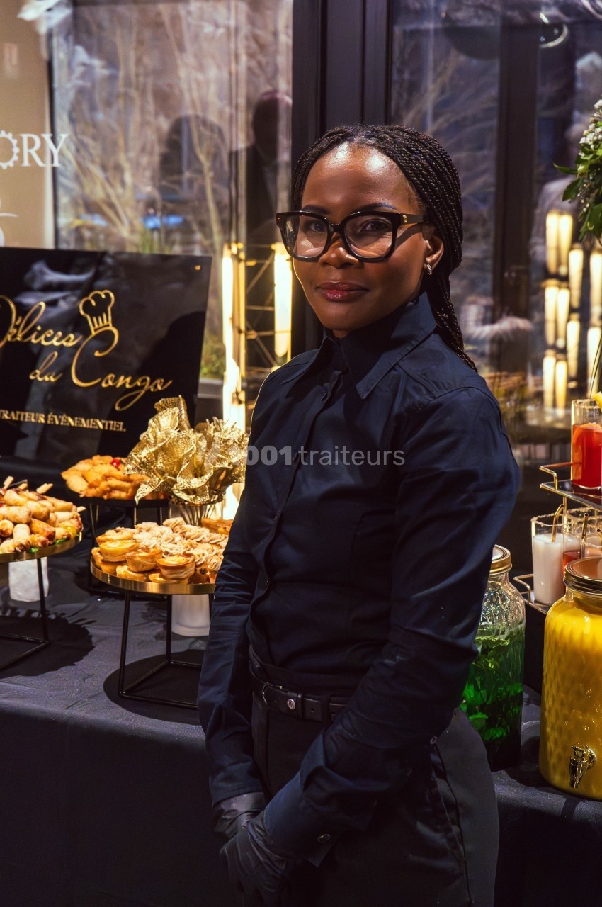 Une femme en tenue professionnelle devant une table garnie de plats et de boissons lors d'un événement.