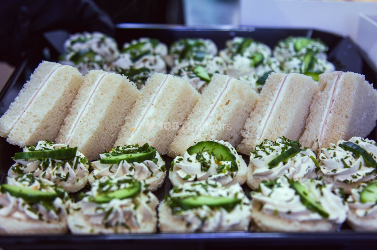Plateau de sandwichs triangulaires et canapés garnis de crème et de tranches de concombre.