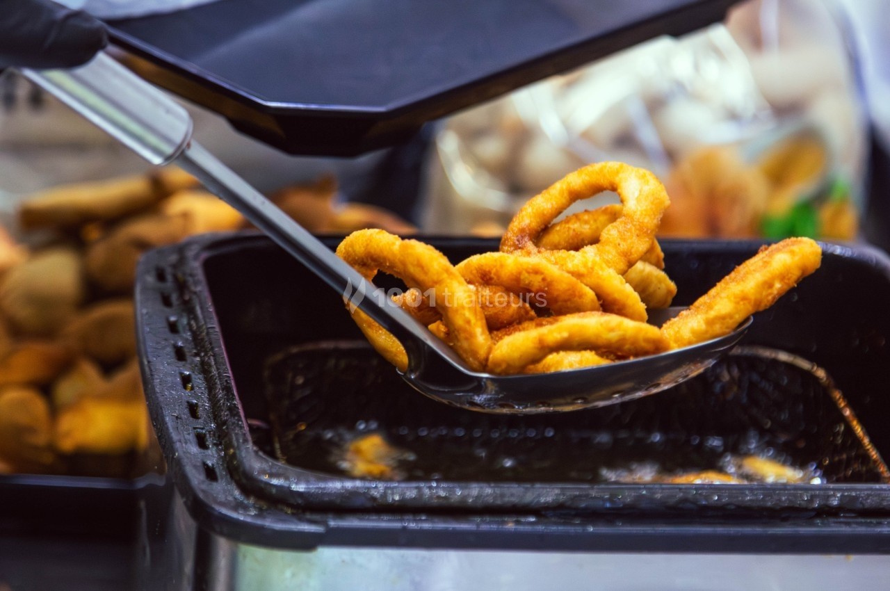 Anneaux d'oignon frits dorés retirés d'une friteuse à l'aide d'une écumoire dans un environnement de cuisine.