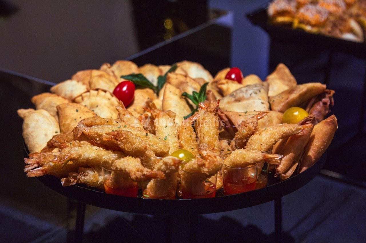 Plateau de bouchées apéritives variées comprenant des crevettes panées, des feuilletés et des légumes décoratifs.