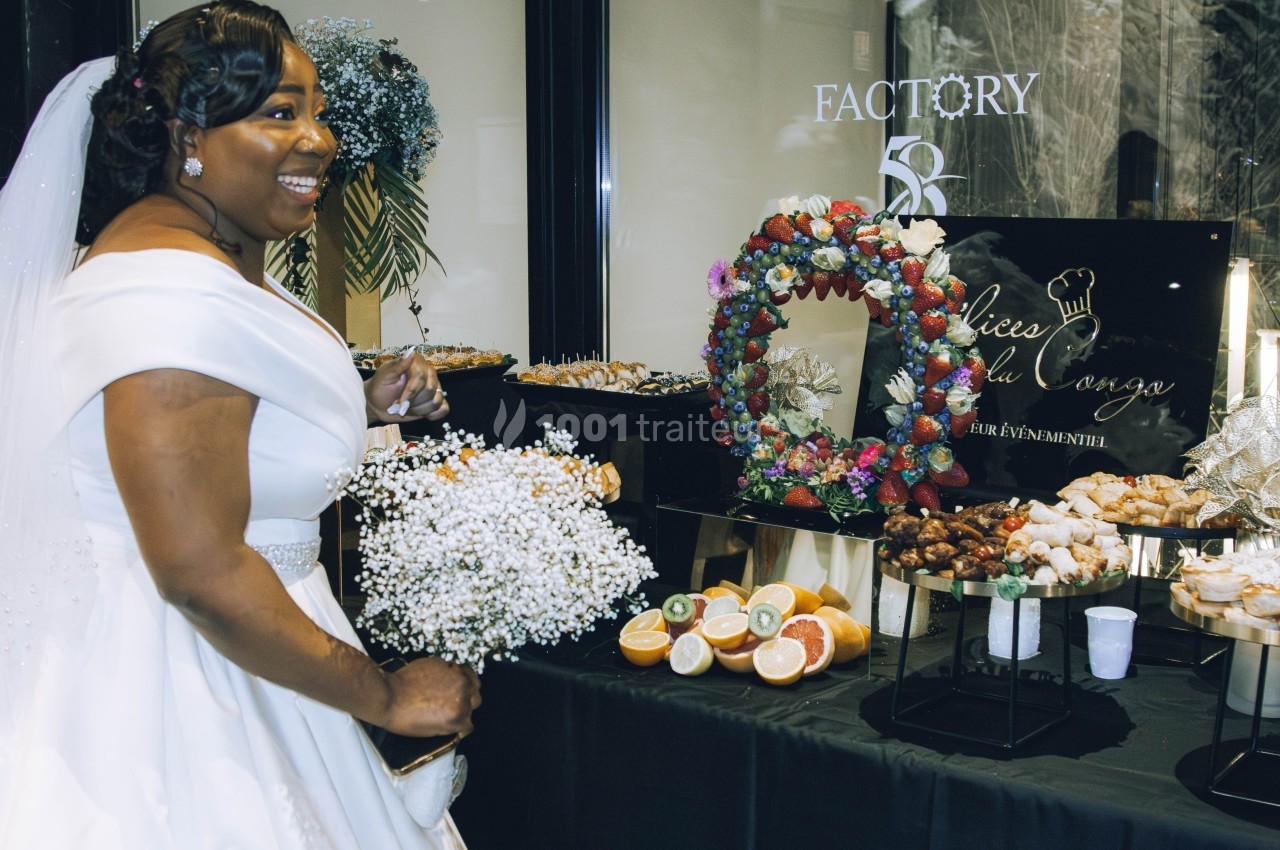 Une mariée souriante en robe blanche près d'une table garnie de desserts et de décorations florales.