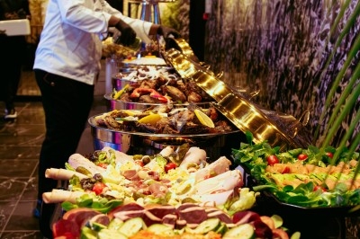 Buffet varié avec plats de viande grillée, légumes frais et charcuterie, présenté dans des plats en métal.