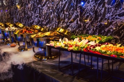 Buffet varié avec plats de viande grillée, légumes frais et charcuterie, présenté dans des plats en métal.