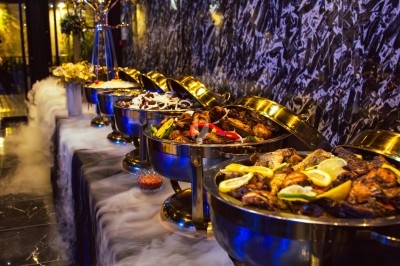 Buffet varié avec plats de viande grillée, légumes frais et charcuterie, présenté dans des plats en métal.