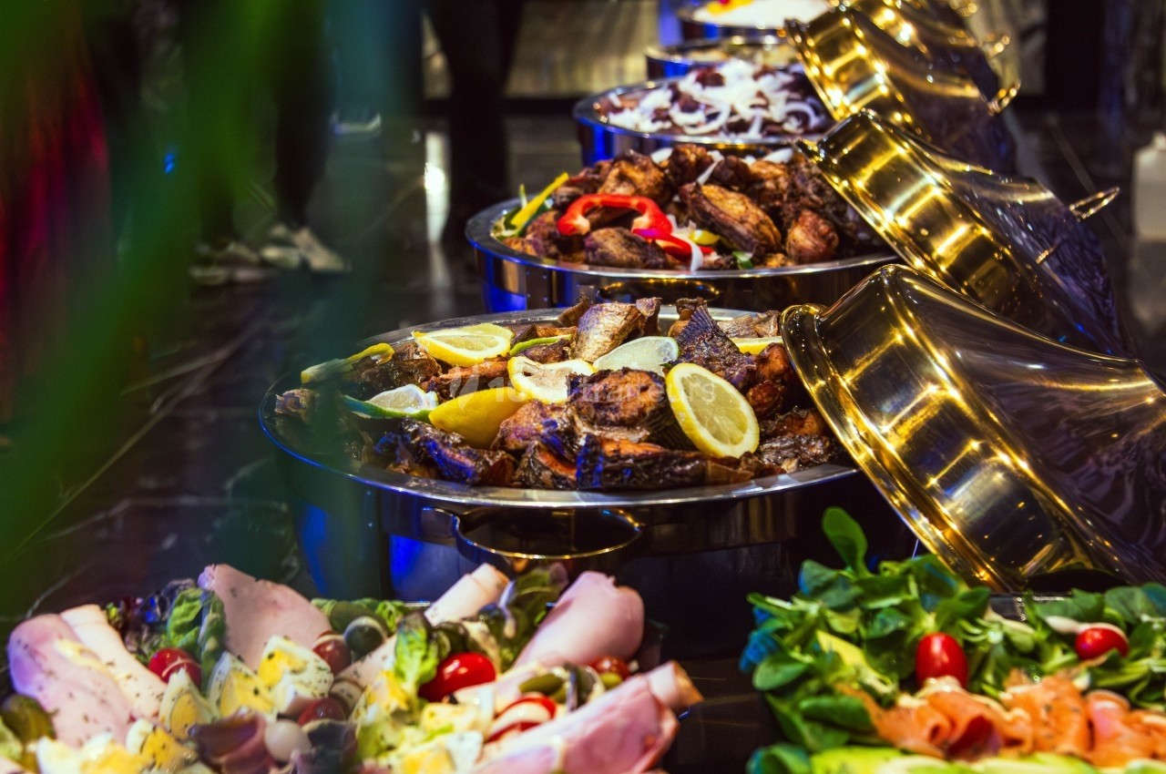 Buffet varié avec plats de viande grillée, légumes frais et charcuterie, présenté dans des plats en métal.