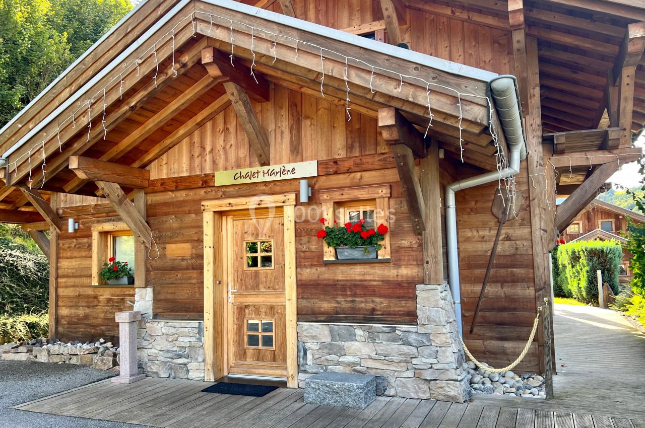 Chalet en bois avec balcon, jardinières fleuries et toit incliné, entouré de végétation.