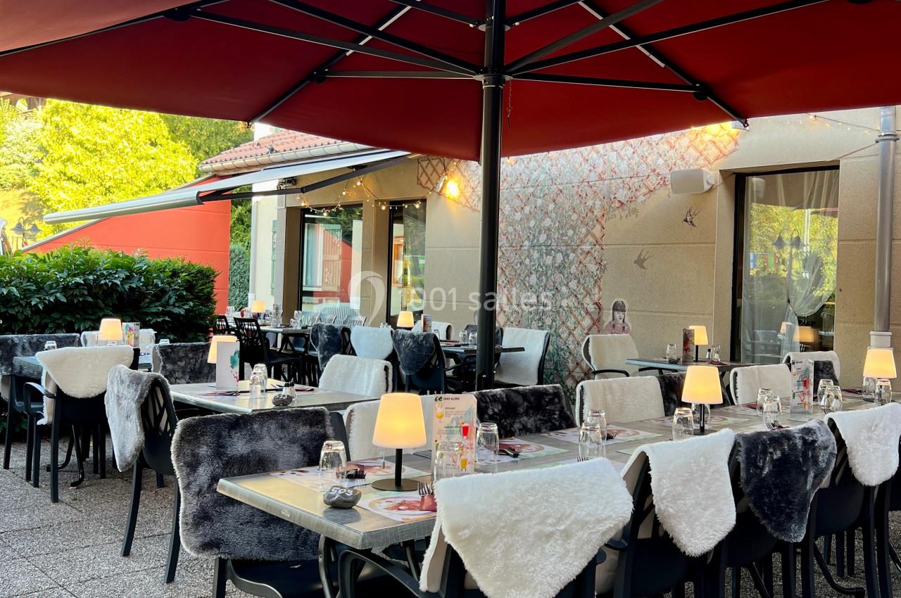 Terrasse d'un restaurant avec tables dressées, chaises couvertes de plaids et grands parasols rouges.