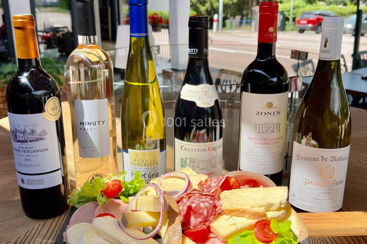 Plateau de charcuterie et fromages avec six bouteilles de vin disposés sur une table en terrasse.